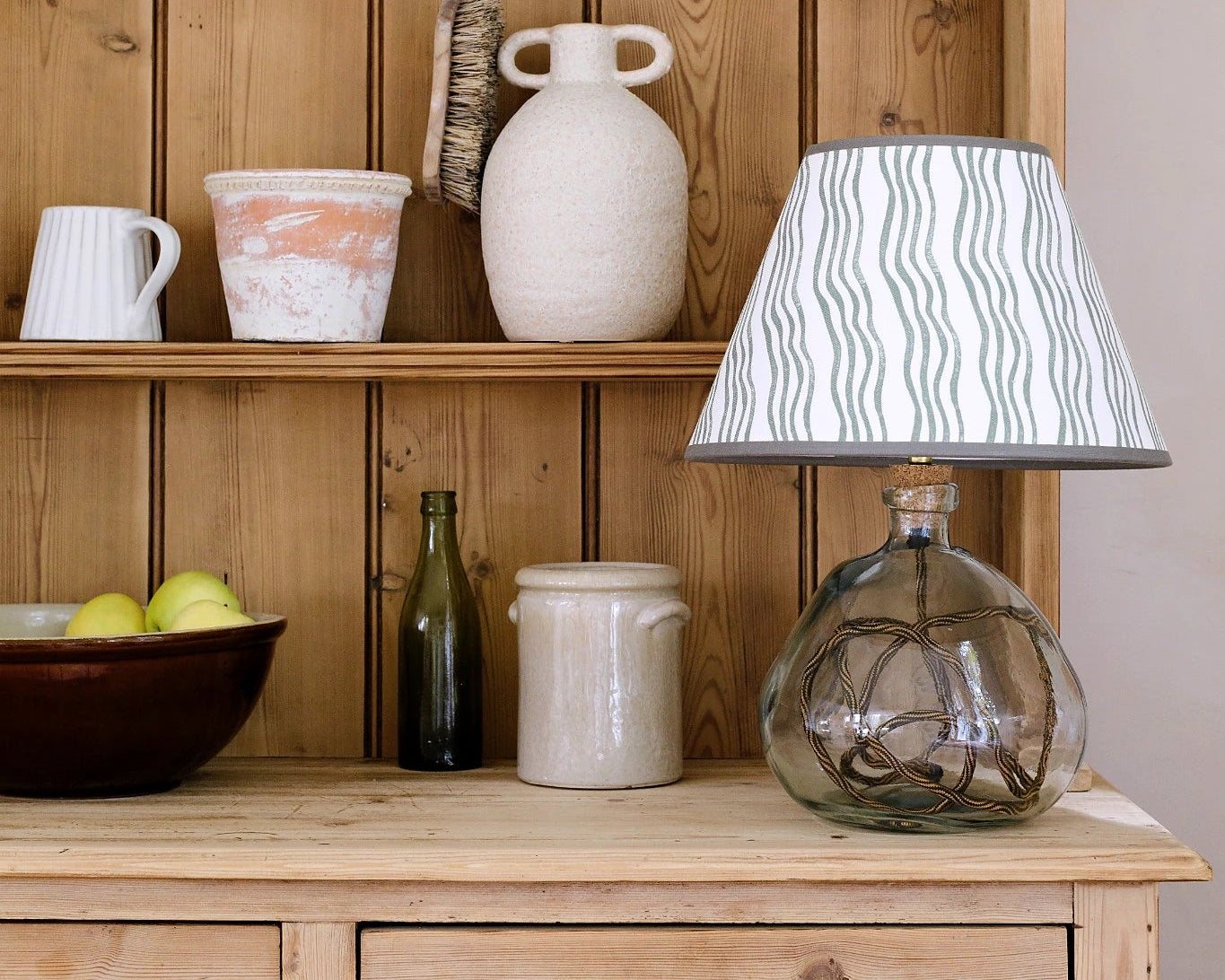 Wooden shelf with various items including a lamp, jars, and a bowl.