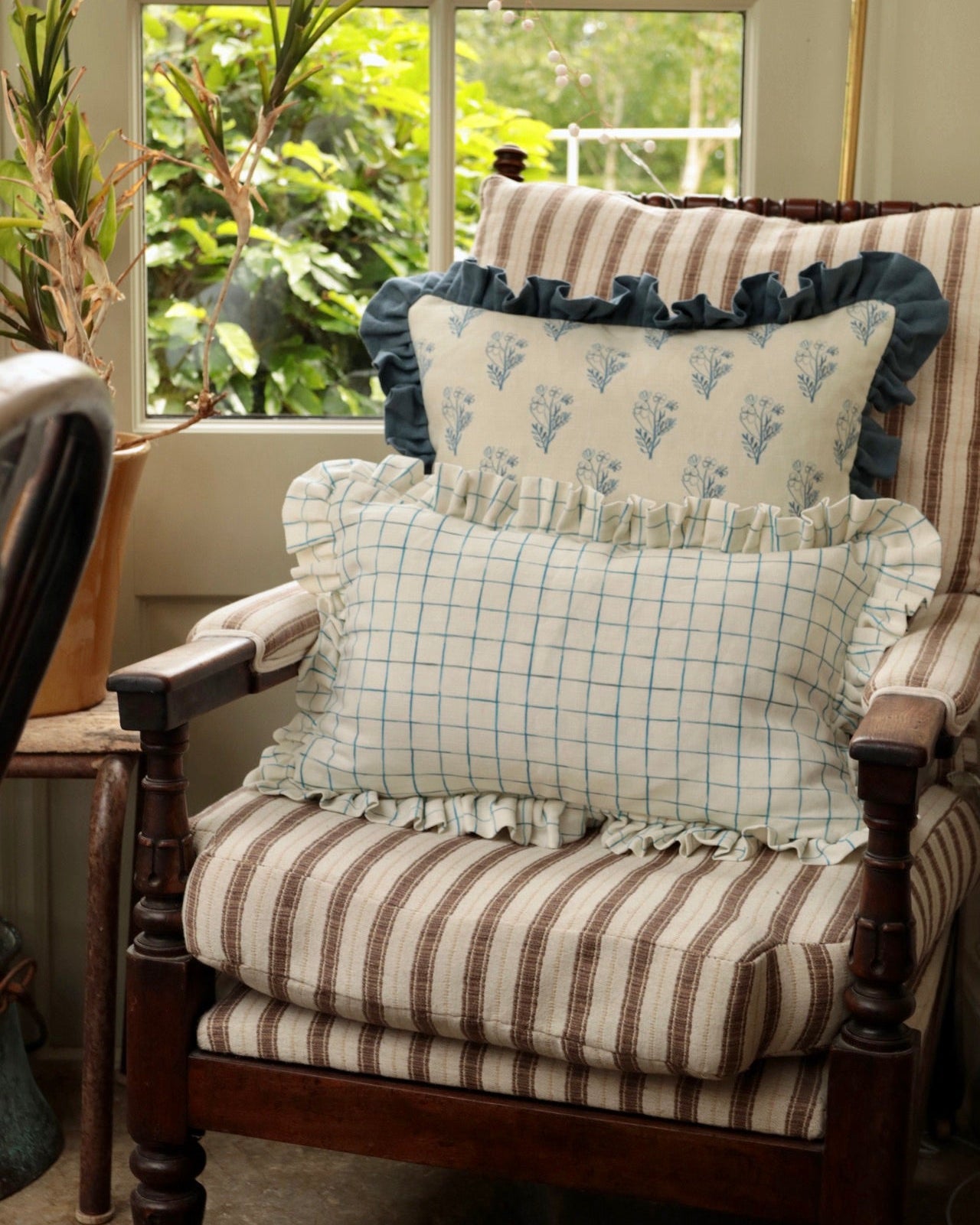 Chair with striped cushions and decorative pillows in a room with a window view of greenery.