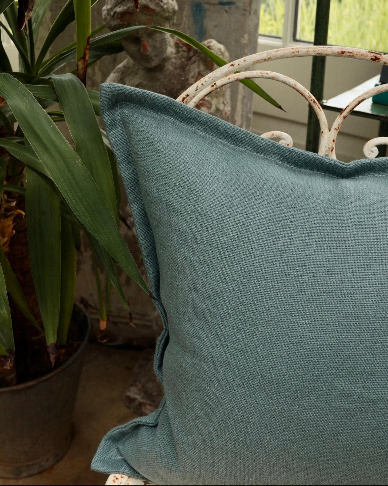 Blue pillow on a chair with plants and a window in the background